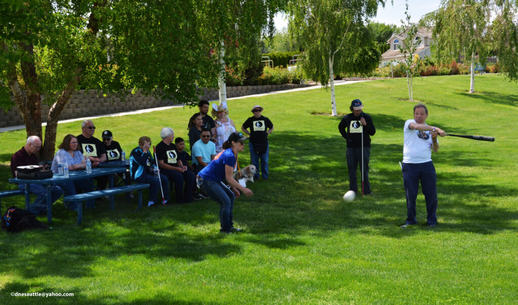 A group of people play beep baseball in a field.