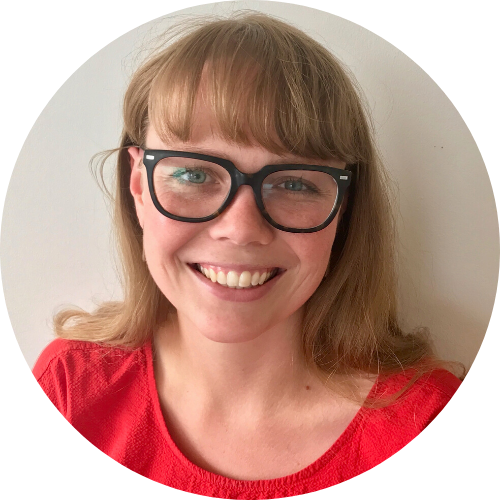 Lianna Olds, a Black woman with black hair and brown eyes and a big smile stands in front of greenery.