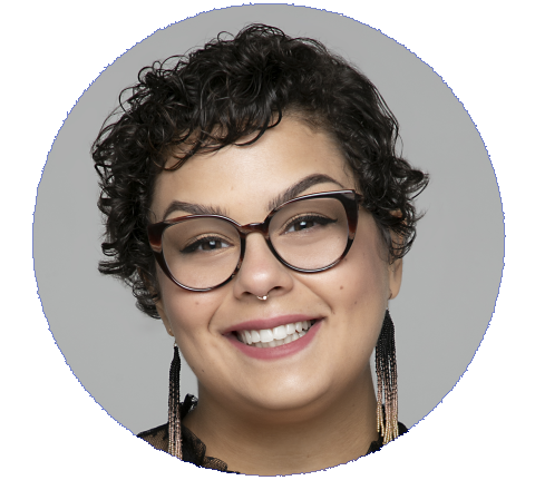 Melodie Garcia a light skinned woman with short curly brown hair, glasses, and a big smile with feather earrings.