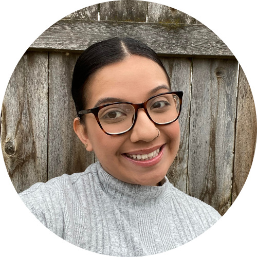 Brissa Perez, a woman with dark brown hair pulled back, eyeglasses, and a big smile, is wearing a grey sweater.